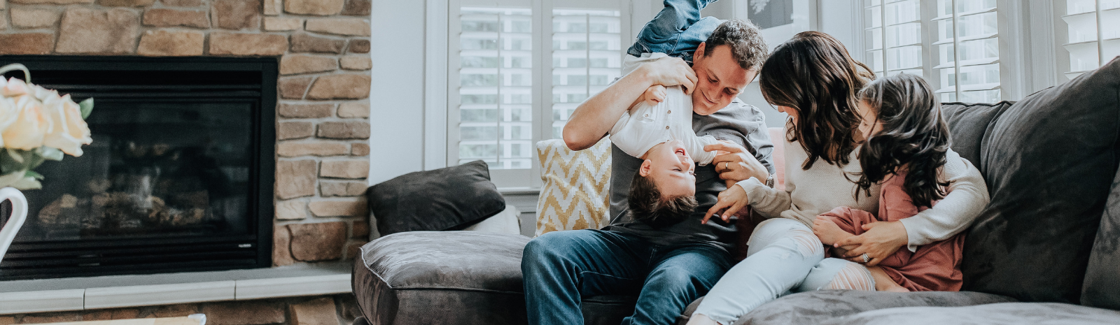 Family with small children playing on a couch in the living room with a fireplace to the left.