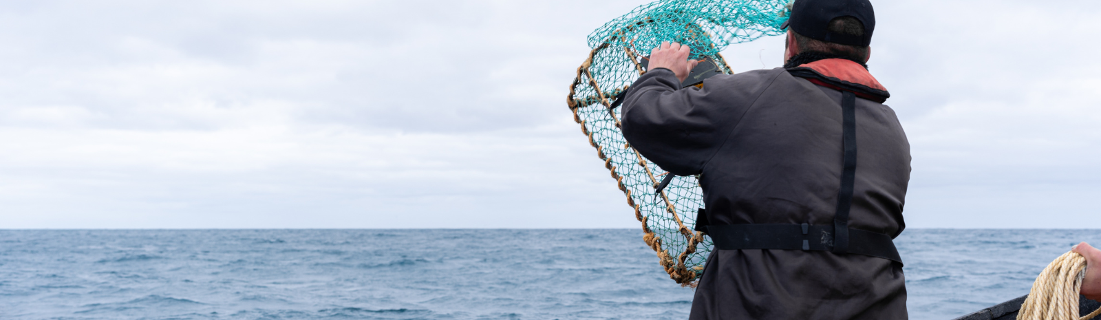 Gloucester fisherman holding a lobster trap while he is on a boat out at sea.