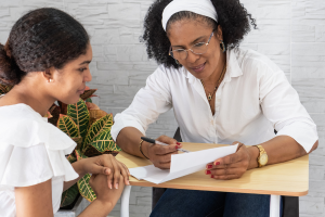 Mom speaking to young daughter showing her something on paper, pointing with pen.