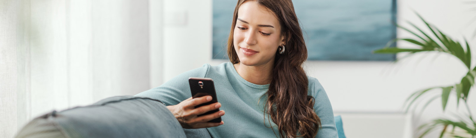 young lady using phone sitting on the couch smiling