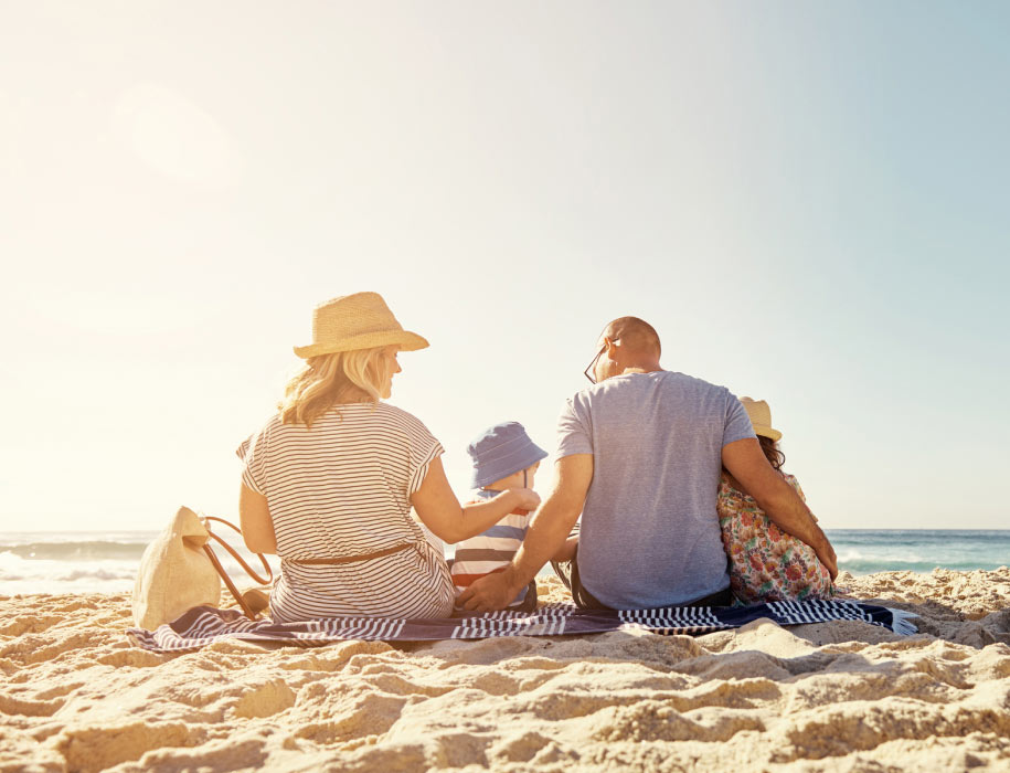 family at the beach, sitting on a towel in the sand